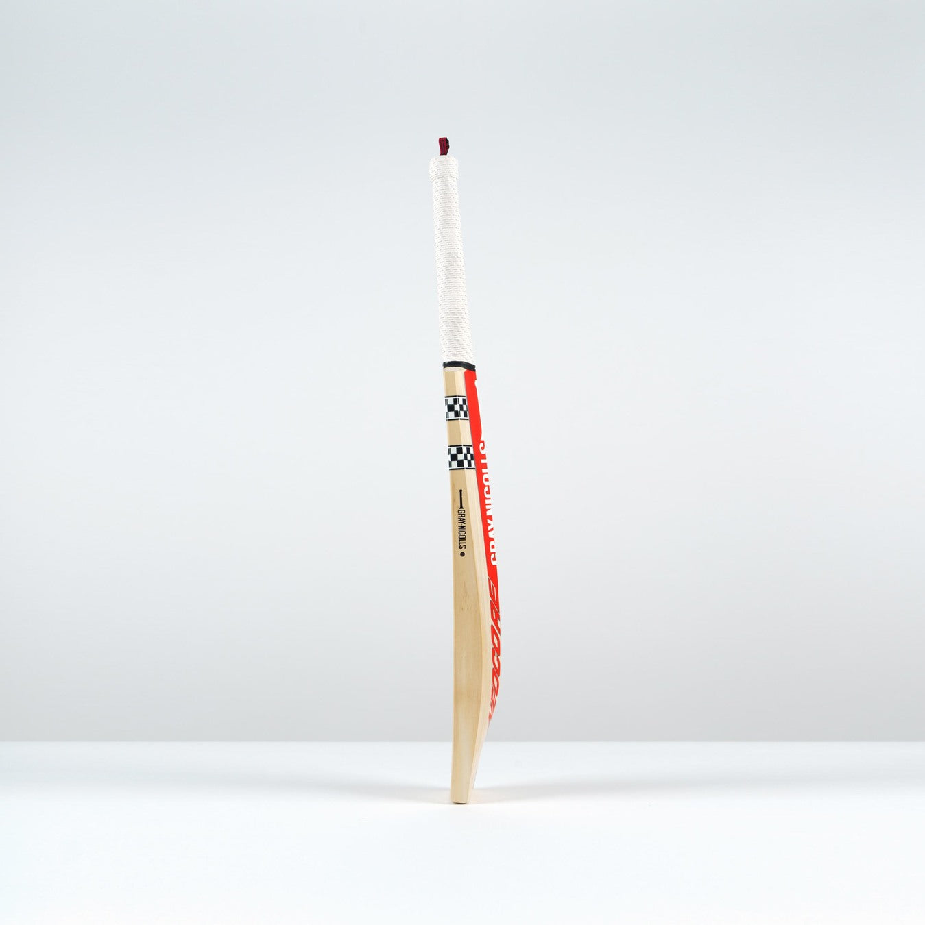 The Gray Nicolls Neocore Pro SH Cricket Bat 2026, showcasing a white handle and checkered design with advanced NEOCORE technology, stands upright on a white surface against a plain, light gray background.