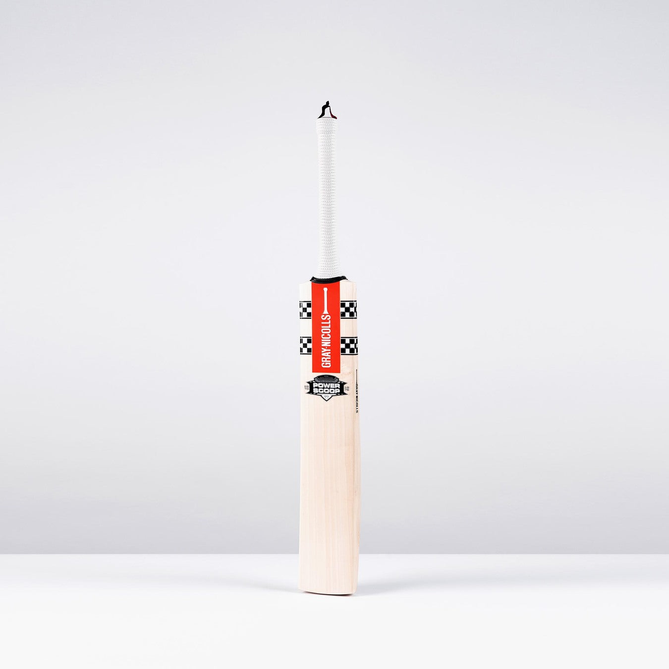 The Gray Nicolls Powerscoop 500 SH Cricket Bat stands upright against a plain light background, featuring a red, black, and white label, a white grip on the handle, and a blade crafted from light-colored wood.