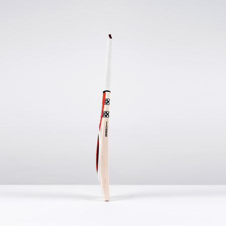 The Gray Nicolls Powerscoop 500 SH Cricket Bat stands upright on a white surface against a light gray background, featuring a wrapped handle and a polished wooden blade with red, black, and white accents.