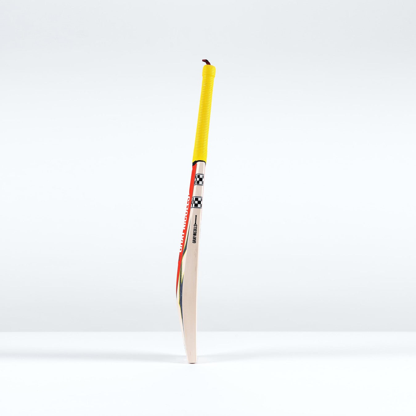 A Gray Nicolls Havoc HB317 Pro Edition SH 2026 cricket bat stands upright on a white surface, showcasing a mid-blade profile, yellow grip, and colorful design near the handle against a plain white background.