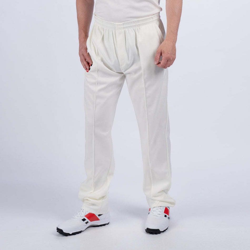 A person wearing Gray Nicolls Quedgeley & Hardwicke CC Matrix V2 Cricket Trousers and white sneakers with red and black accents stands against a plain light background, with only the lower body visible.