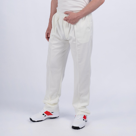 A person wears Gray Nicolls Matrix V2 Match Trousers and white sneakers with red and black accents, standing against a plain white background. Only the lower torso and legs are visible.
