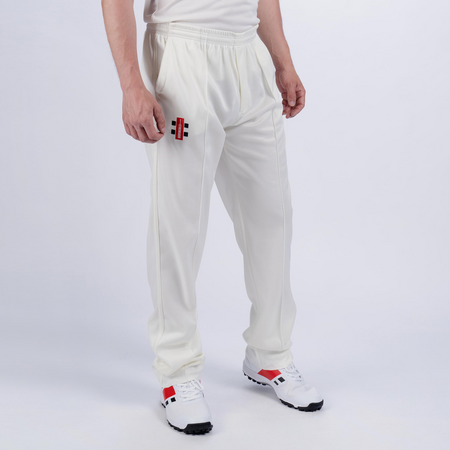 A person wearing Gray Nicolls Matrix V2 Match Trousers, a white shirt, and white sports shoes with red and black accents, stands against a plain white background.