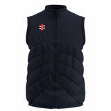 The Gray Nicolls Old Down CC GTS Body Warmer is a dark navy, sleeveless cricket vest with a front zipper, high collar, horizontal quilted stitching, and a small red, white, and black rectangular logo on the left chest. Lightweight comfort.