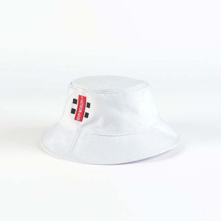 The Gray Nicolls Bucket Hat by Gray Nicolls is a white hat featuring a red vertical tag with black and white text and two sets of double black square designs on the front, shown against a plain white background.