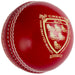 A close-up of the Gray Nicolls Crest Elite Cricket Ball, featuring shiny red chrome tanned leather with white stitching and a gold embossed Crest Elite Hand Crafted Quality logo beside an emblem with six birds.
