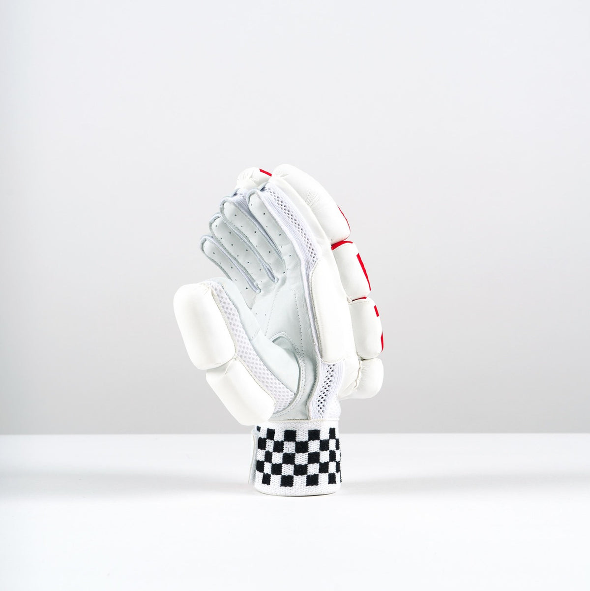A single Gray Nicolls Neocore 500 Batting Glove stands upright on a white surface. It features tri-layer protection, padded fingers and knuckles, red accents, and a black-and-white checkered wristband against a light gray background.