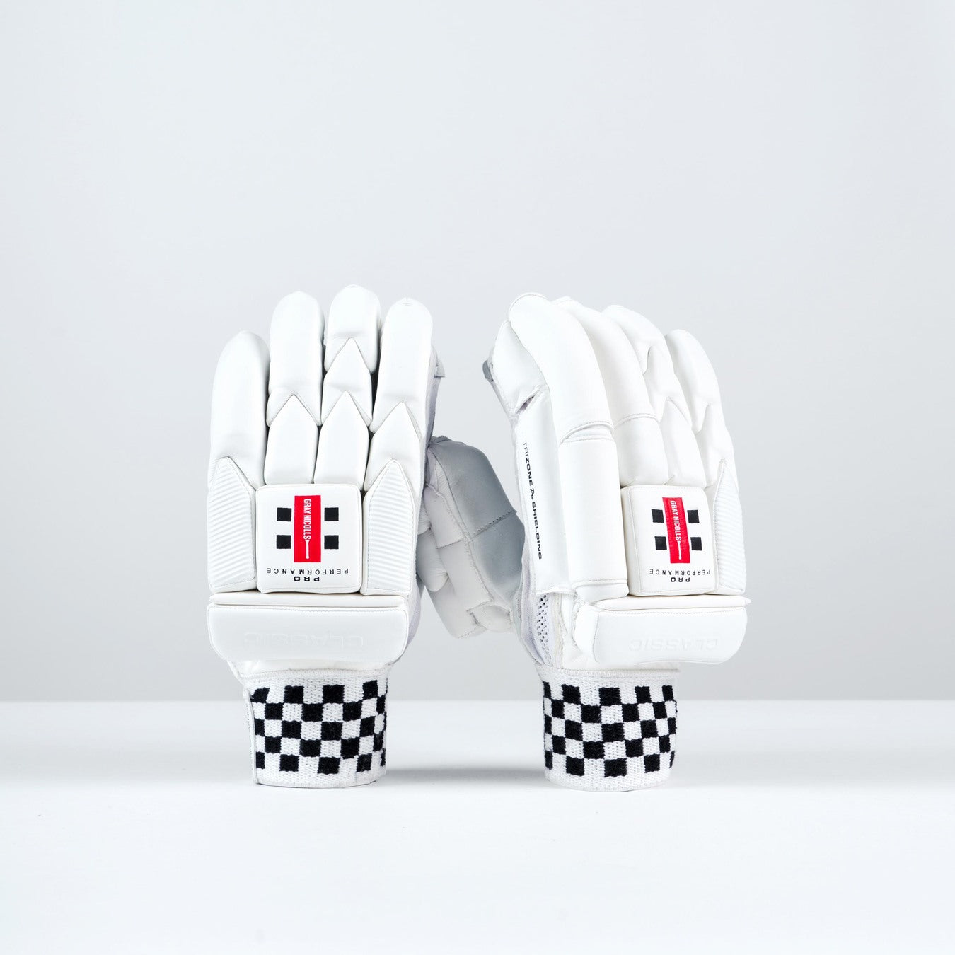 The Gray Nicolls Pro Performance Batting Gloves 2026 stand upright on a white surface, featuring black and white checkered wristbands and red logos, highlighting the classic design of these premium cricket gloves by Gray Nicolls.