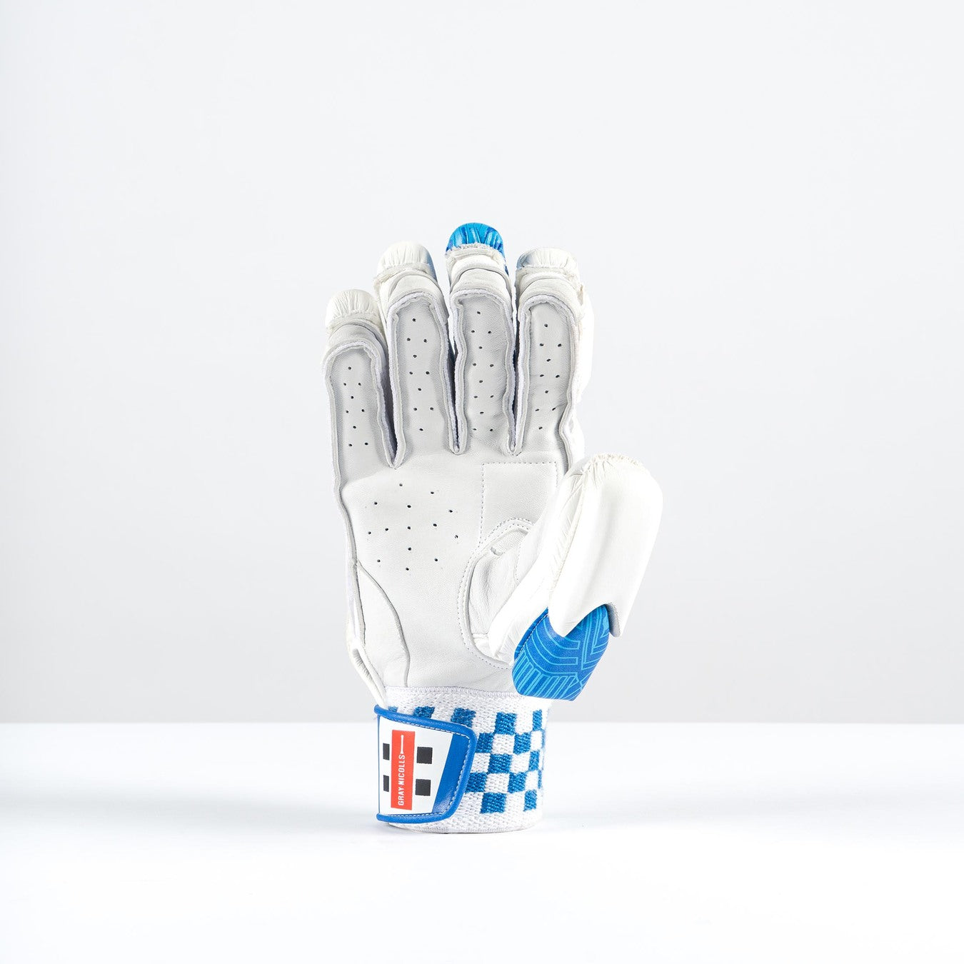The Gray Nicolls Havoc 1.0 1000 Batting Gloves 2026 stands upright on a white surface, showcasing white with blue accents, split-finger design, high-density foam padding, and a checkered wrist strap against a plain light background.
