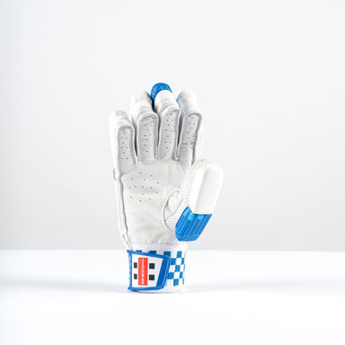The Gray Nicolls Havoc 1.0 700 Batting Gloves 2026 stands upright, featuring white and blue colors, curved fingers for protection, perforations, blue accents, and a red-and-white patch on the wrist strap.