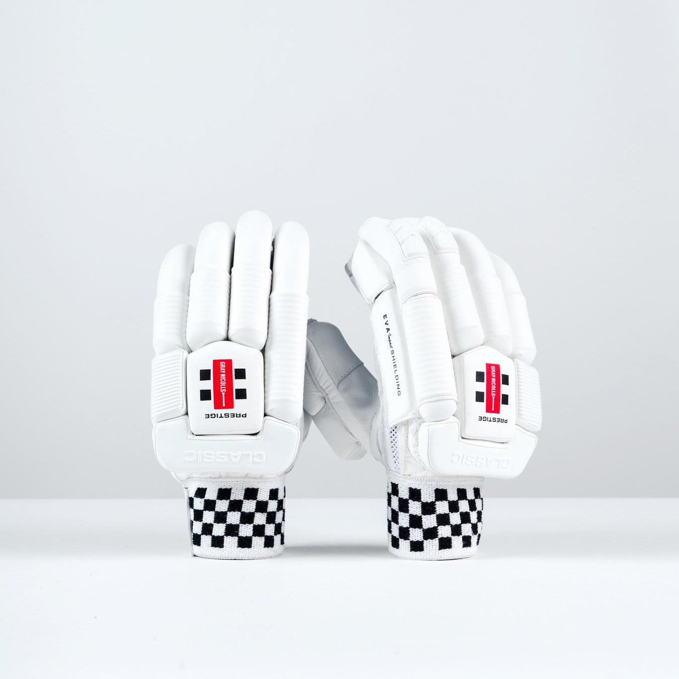 Two Gray Nicolls Classic Prestige Batting Gloves 2026 with black-and-white checkered wristbands stand upright, showing a red and black logo, "PROTECTION" print, enhanced finger protection, and leather palms for superior grip.