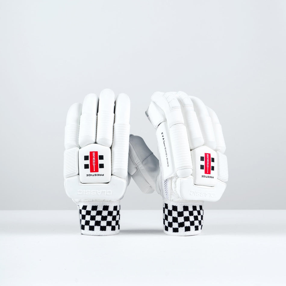 Two Gray Nicolls Classic Prestige Batting Gloves 2026 with black-and-white checkered wristbands stand upright, showing a red and black logo, "PROTECTION" print, enhanced finger protection, and leather palms for superior grip.