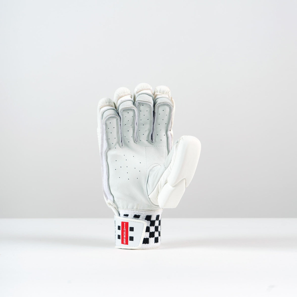 A single Gray Nicolls Classic Prestige Batting Glove 2026 stands upright on a white surface, palm forward. It features a durable leather palm, black ventilation holes, finger padding, and a red and black checkered wrist strap.