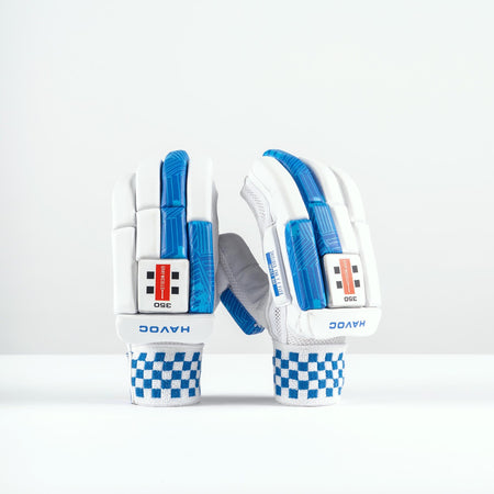 A pair of Gray Nicolls Havoc 1.0 350 Batting Gloves 2026 in white with blue accents and checkered wristbands stand upright on a white surface, showing finger protection and the Gray Nicolls brand name on the wrist.