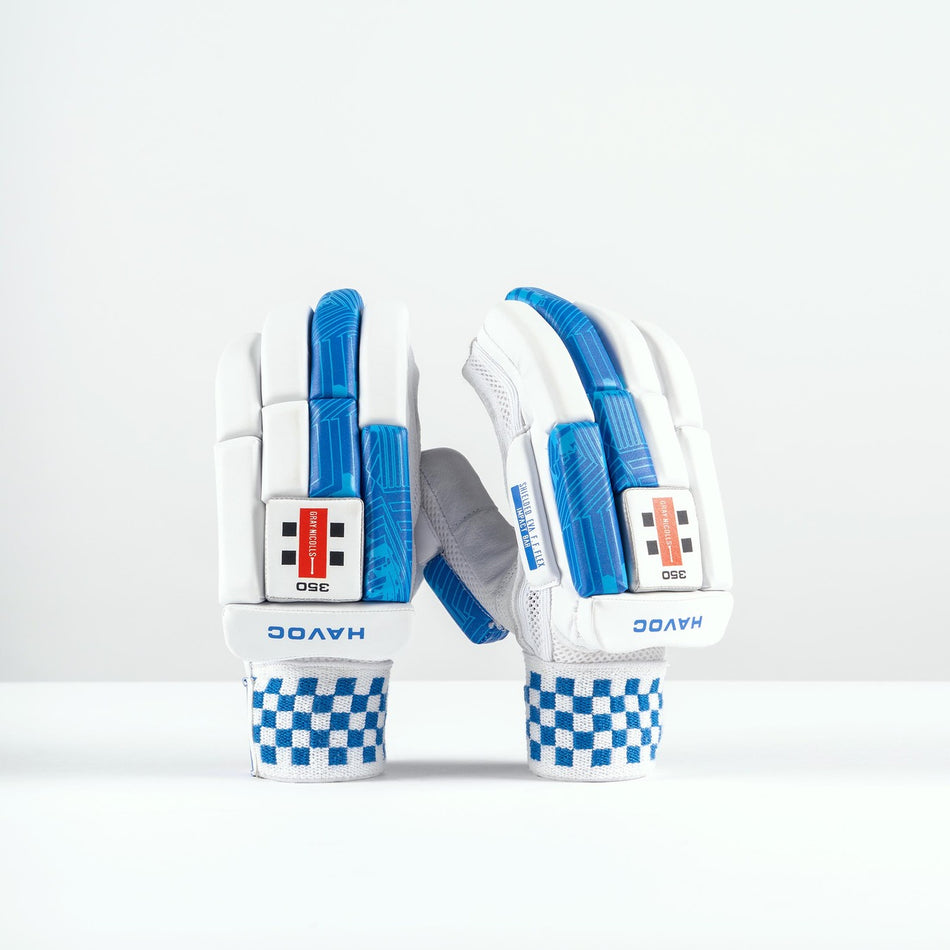 A pair of Gray Nicolls Havoc 1.0 350 Batting Gloves 2026 in white with blue accents and checkered wristbands stand upright on a white surface, showing finger protection and the Gray Nicolls brand name on the wrist.
