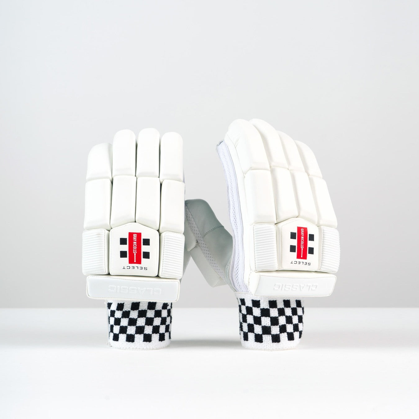 A pair of Gray Nicolls Classic Select Batting Gloves 2026 with black and white checkered wrists, leather palm for grip, and red SELECT logos are displayed upright on a white surface against a plain light background.