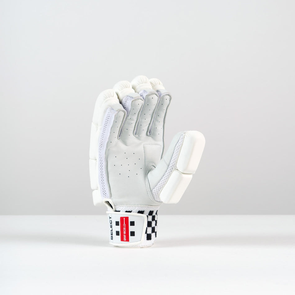 The Gray Nicolls Classic Select Batting Gloves 2026 stand upright on a light gray background, showcasing white padding, finger protection, perforations, mesh accents, a leather palm, and a wrist strap with a red and black checkered label.