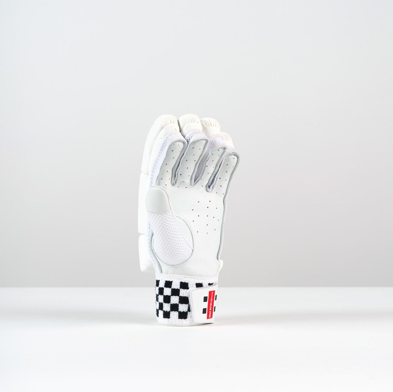 The Gray Nicolls Classic Academy Batting Gloves 2026 by Gray Nicolls feature a white design with gray accents, black perforations, high density foam padding, and a black-and-white checkered wrist strap displayed upright on a light gray background.