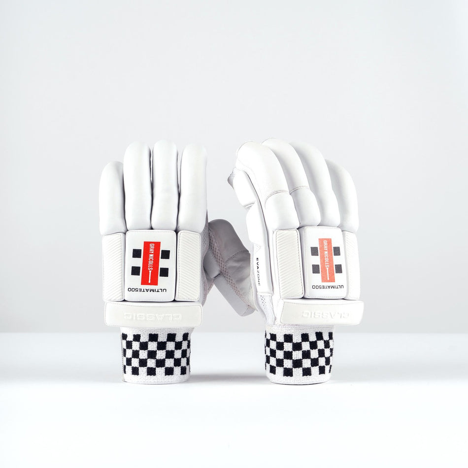 The Gray Nicolls Ultimate 500 Batting Gloves 2026 are white cricket gloves with tri-layer protection, padded fingers, black-and-white checkered wristbands, and a red and black wrist label, shown upright on a plain white background.
