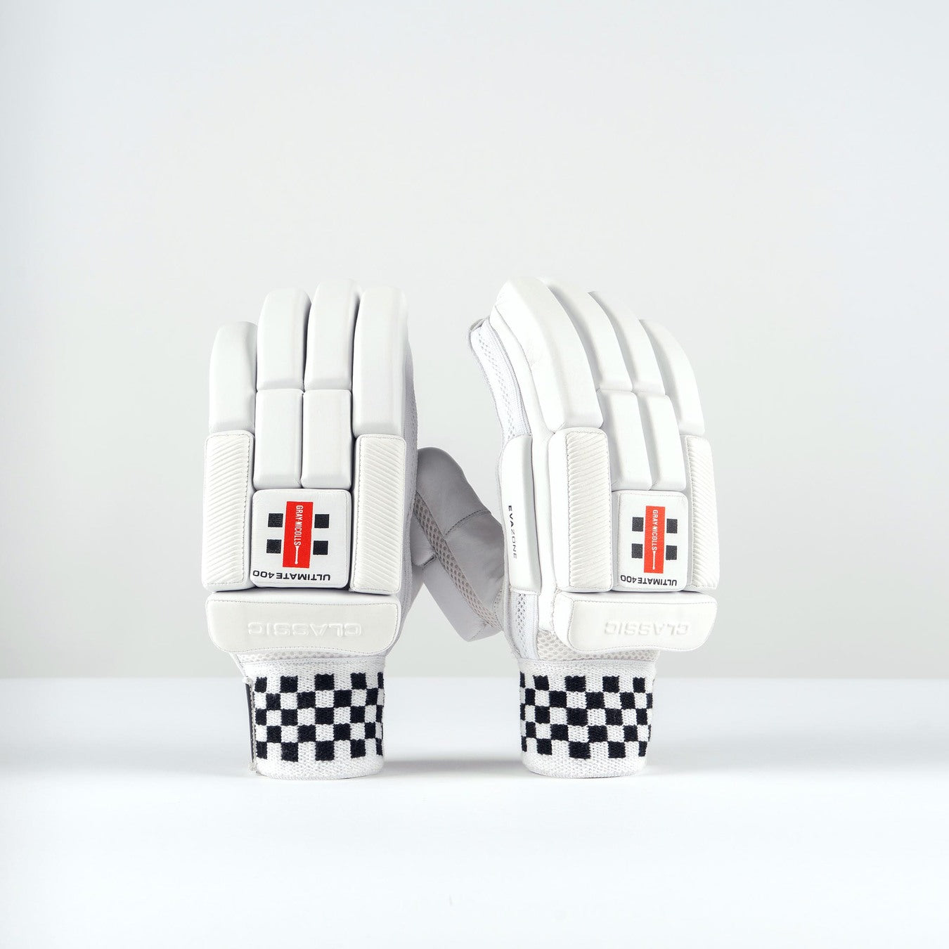 The Gray Nicolls Classic Ultimate 400 Batting Gloves 2026 stand upright, showing white design with high-density foam padding on fingers and knuckles, plus striking red and black wrist detailing and black-and-white checkered wristbands.