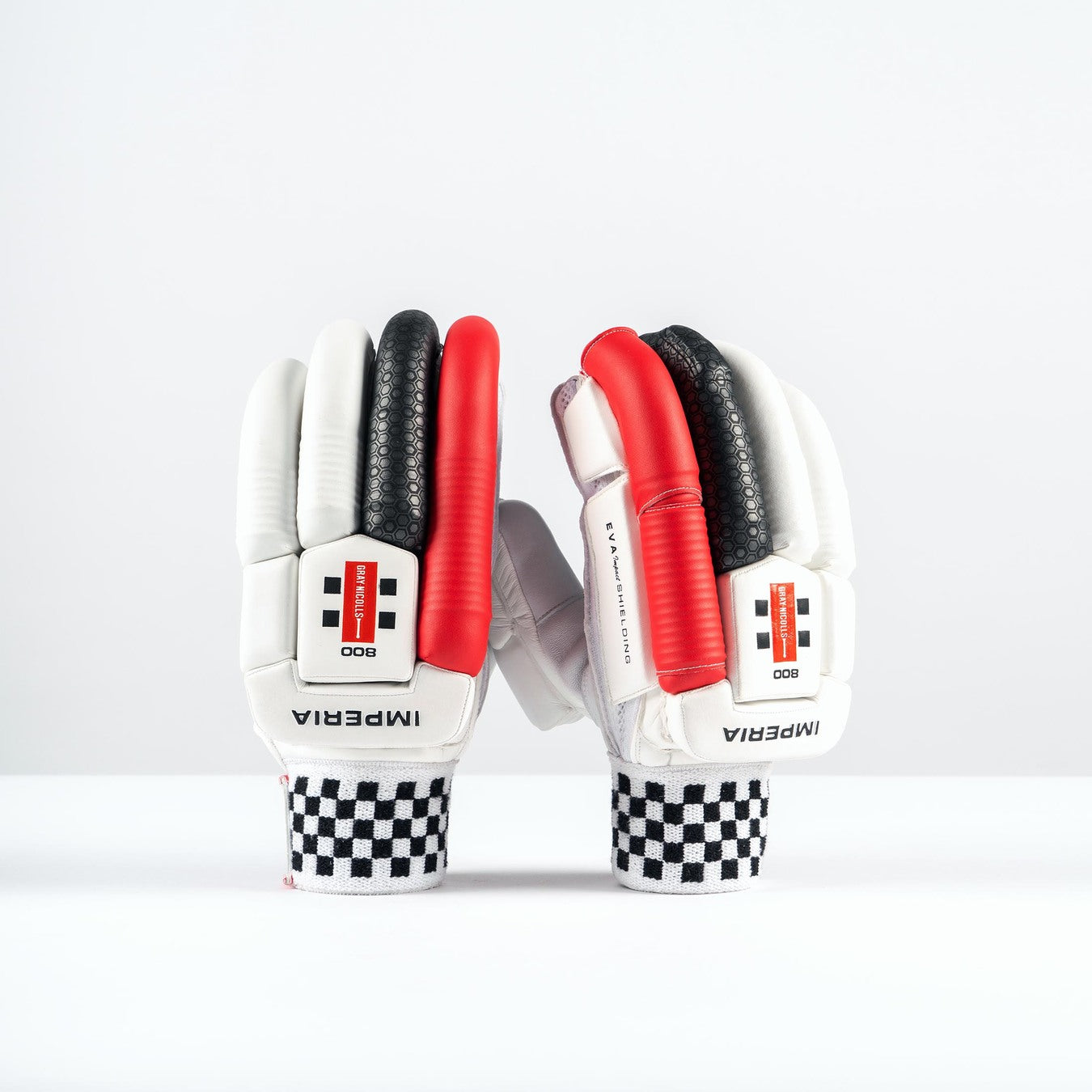 The Gray Nicolls Imperia 1.0 800 Batting Gloves 2026 stand upright on a white surface, showcasing checkered wristbands and bold Gray Nicolls branding in white, black, and red, displayed facing forward with minimal background detail.