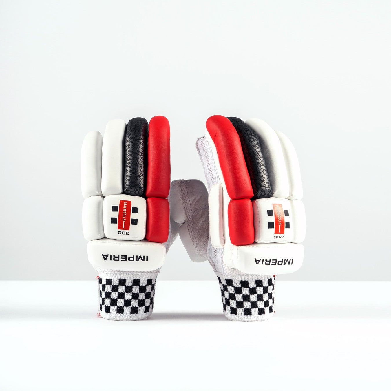The Gray Nicolls Imperia 1.0 300 Batting Gloves 2026 feature white padded fronts, red and black accents, and checkered black-and-white cuffs with the brand name “IMPERIA.” Ideal junior gloves for club cricket, shown upright on a white surface.