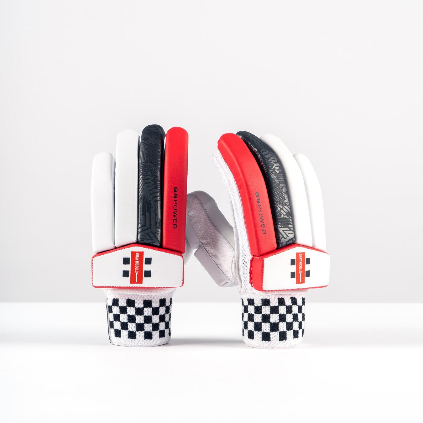 The Gray Nicolls GN PowerX Batting Gloves 2026, in white, black, and red with black-and-white checkered cuffs, stand upright against a plain white background. The entry-level gloves feature a modern sporty design and graphic details on the fingers.