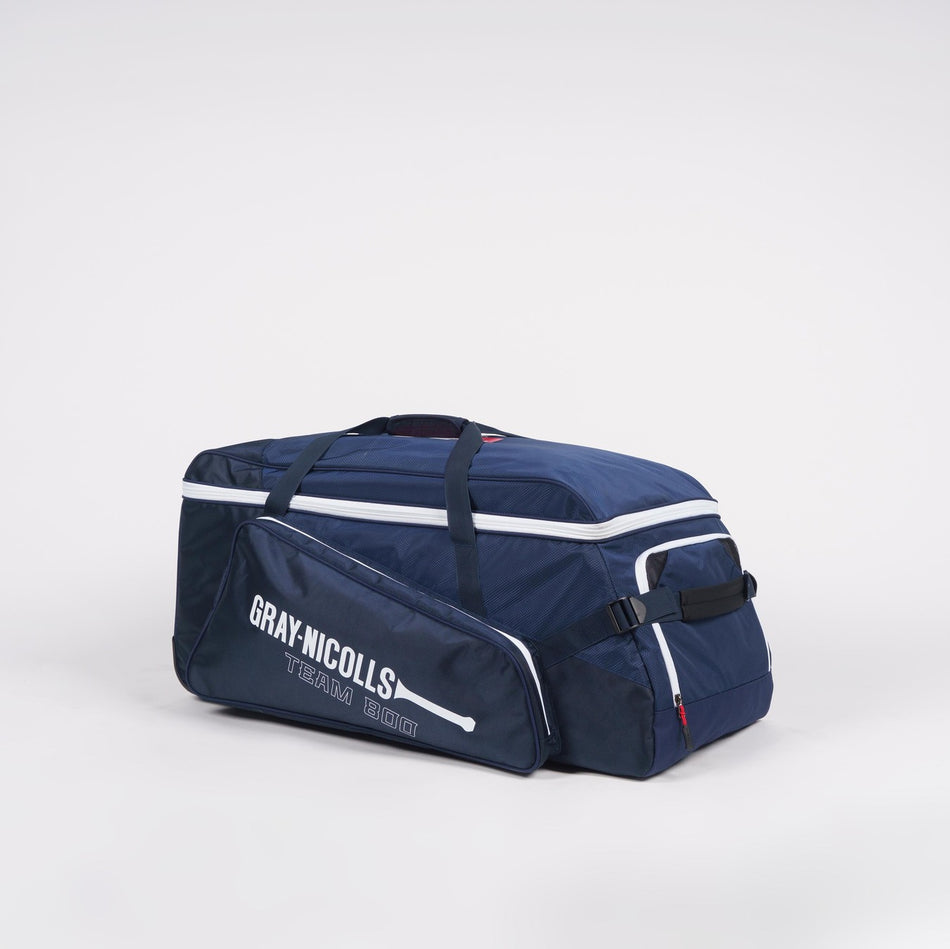 A Gray Nicolls Team 800 Wheelie cricket kit bag in navy blue with white piping, featuring large storage, zippered compartments, wheels, and carry handles, displayed against a plain white background.
