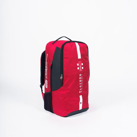 A small red Gray Nicolls Players Academy Duffle 2026 sports backpack with a top handle and zippered compartments, featuring white "Players Academy" and "Gray Nicolls" text on the front, shown against a plain white background.