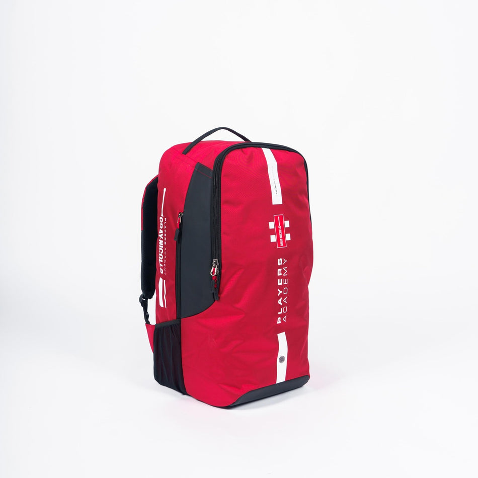 A small red Gray Nicolls Players Academy Duffle 2026 sports backpack with a top handle and zippered compartments, featuring white "Players Academy" and "Gray Nicolls" text on the front, shown against a plain white background.
