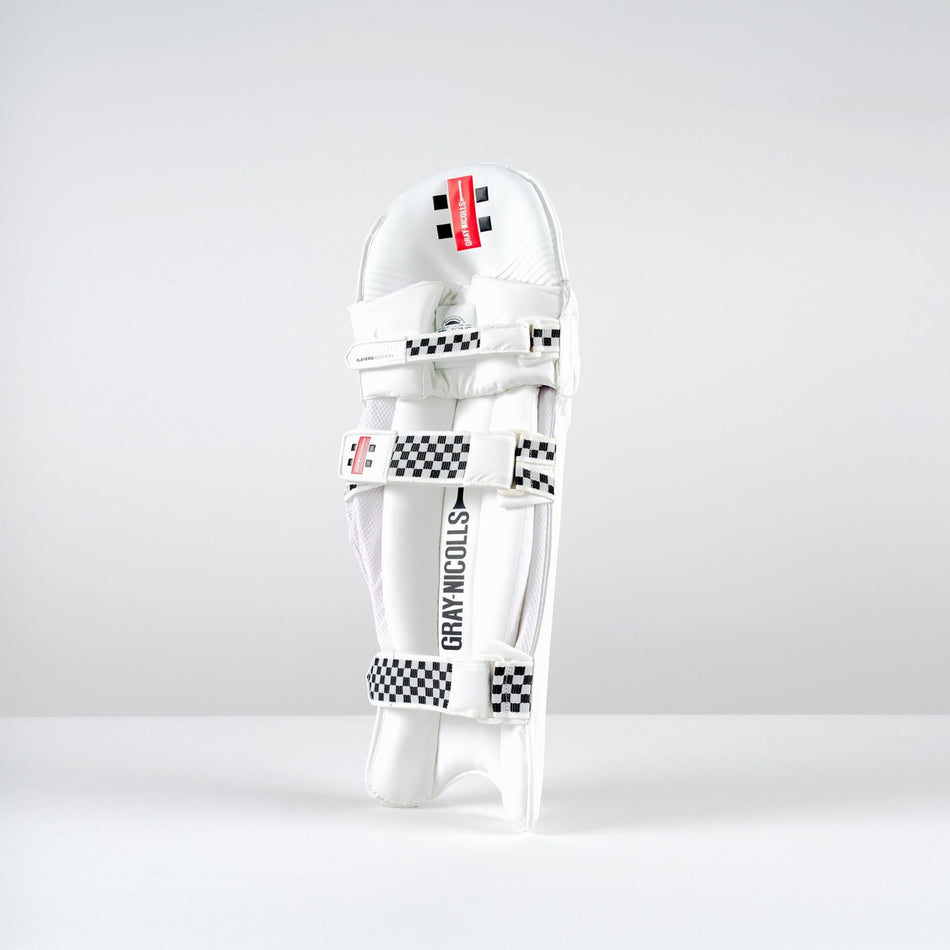 A Gray Nicolls Classic Players Edition Batting Pad 2026 stands upright on a white surface, featuring black-and-white checkered straps, a red label, and lightweight HDF multilayer protection against a plain light gray background.