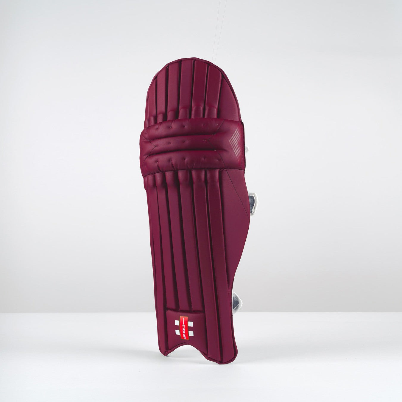 The Gray Nicolls Classic Select Batting Pads 2026 in maroon stand upright on a white surface with a light gray background, featuring horizontal and vertical padding lines for lightweight comfort and HDF EVA protection.