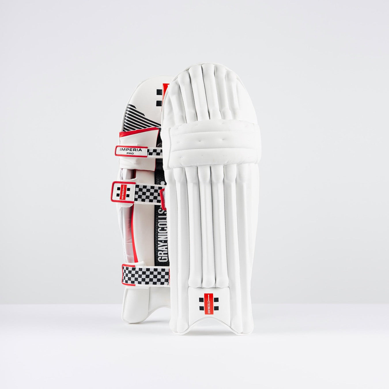 The Gray Nicolls Imperia 1.0 Pro Batting Pads 2026 feature red and black accents with checkered patterns, offering professional cricket protection, shown standing upright against a plain white background.
