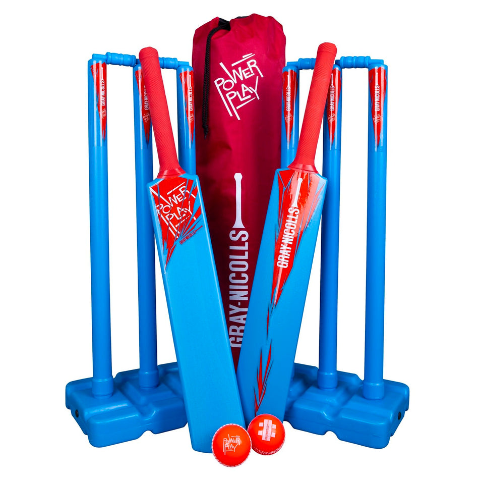 The Gray Nicolls PowerPlay Blue Kit includes two blue and red bats, two sets of blue stumps with stands, two orange balls, and a red carrying bag—ideal for kids’ cricket matches outdoors.