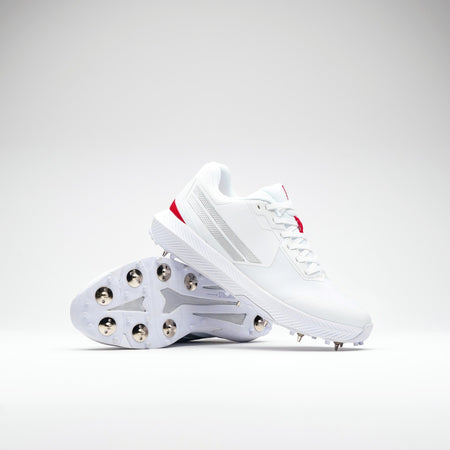 The Gray Nicolls Revo Pro 2.0 Cricket Spikes by Gray Nicolls feature white uppers with silver and red accents, a Maxcool Duo upper, Energise midsole, and metal studs. One shoe stands upright while the other shows the studded sole.