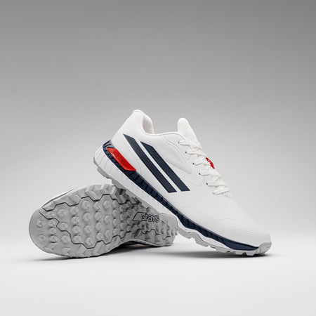 The Gray Nicolls Revo Pro 3 Cricket Batting Shoe features a white upper with dark blue stripes, red accents, and textured gray soles. One shoe stands upright while the other lies on its side to display the tread pattern.