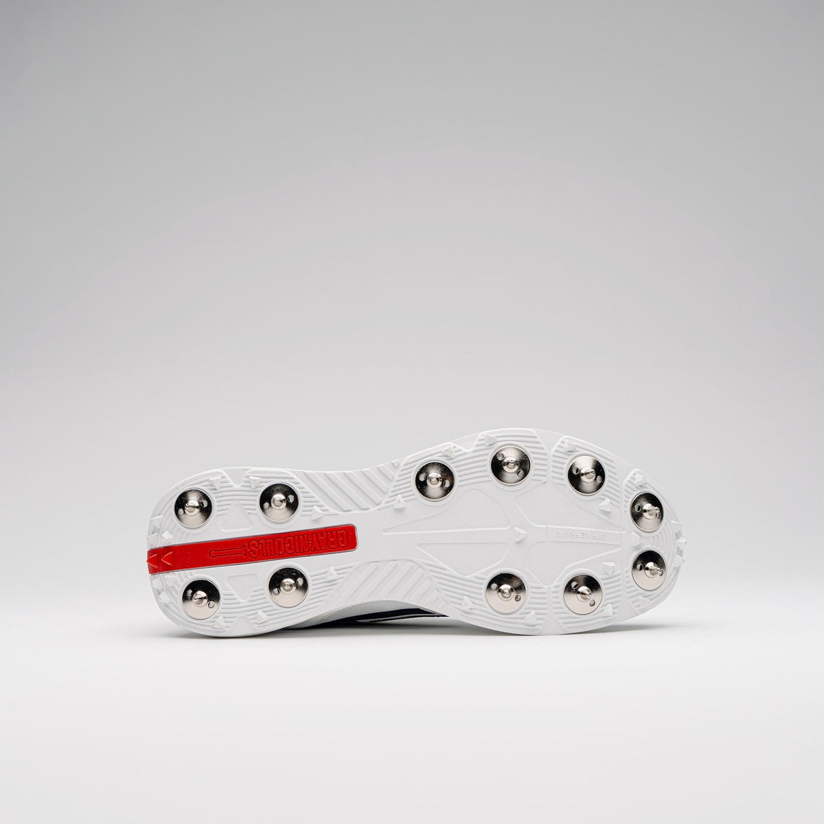 The underside of a white Gray Nicolls Players 4.0 Cricket Spikes shoe with metal studs and a red rectangular “Gray Nicolls” logo on the sole, shown against a plain light gray background.