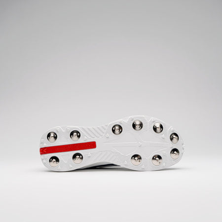 The underside of a white Gray Nicolls Players 4.0 Cricket Spikes shoe with metal studs and a red rectangular “Gray Nicolls” logo on the sole, shown against a plain light gray background.