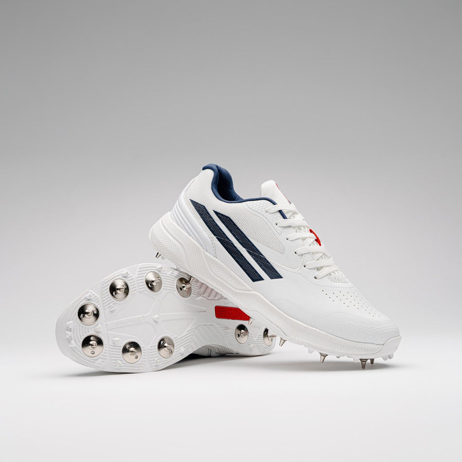 The Gray Nicolls Players 4.0 Cricket Spikes, premium white footwear with metal spikes, navy blue stripes, and red accents by Gray Nicolls, are shown against a plain light gray background.