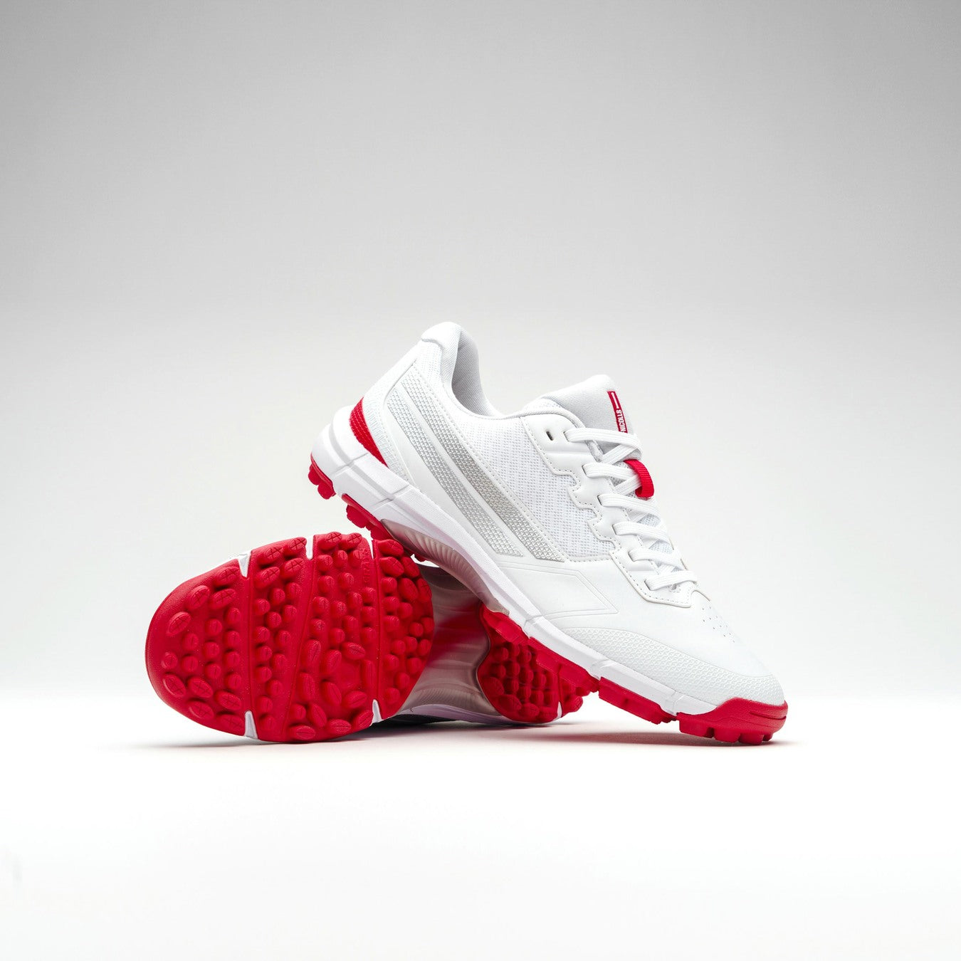 The Gray Nicolls Velocity 5.0 Rubber Sole Cricket Shoe features a white design with red accents and textured red rubber soles. One shoe stands upright while the other leans against it, all set against a plain light gray background.