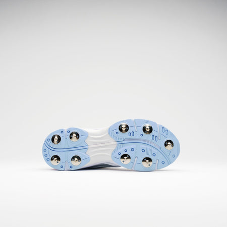 The image displays the bottom view of Gray Nicolls Velocity 5.5 Narrow Cricket Spikes, featuring a white sole with light blue accents and six round metal studs on each side, set against a plain white background.