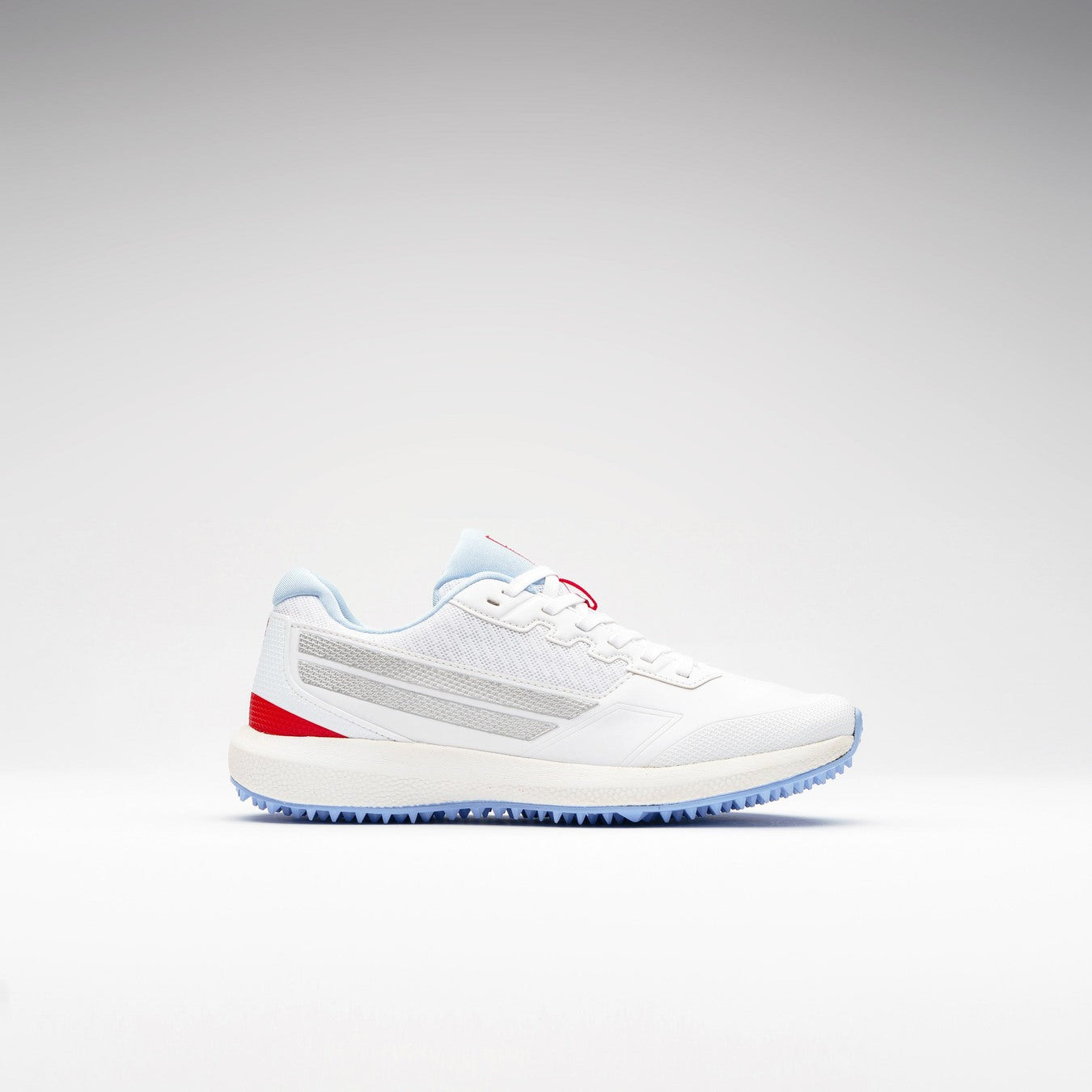 The Gray Nicolls Velocity 5.5 Narrow Rubber Soled Cricket Shoe for women features a white mesh upper, light blue accents, red heel details, and a textured blue rubber sole—offering style, comfort, and a perfect narrow fit. Displayed on plain white background.