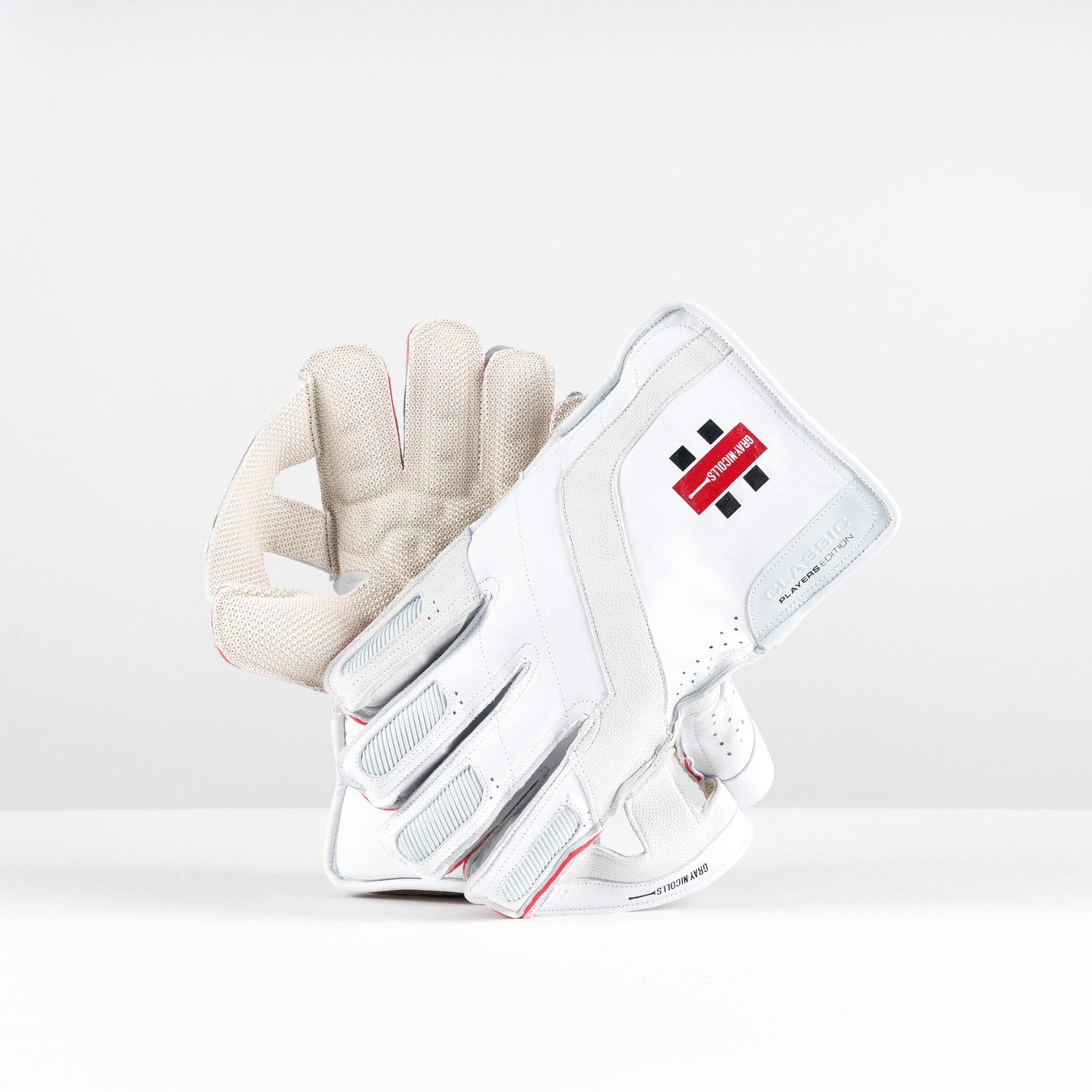 The Gray Nicolls Classic Players Edition WK Gloves 2026, premium leather gloves in white, are displayed upright on a plain white background. One shows the palm with octopus grip; the other displays the back, featuring a logo and subtle red and black accents.
