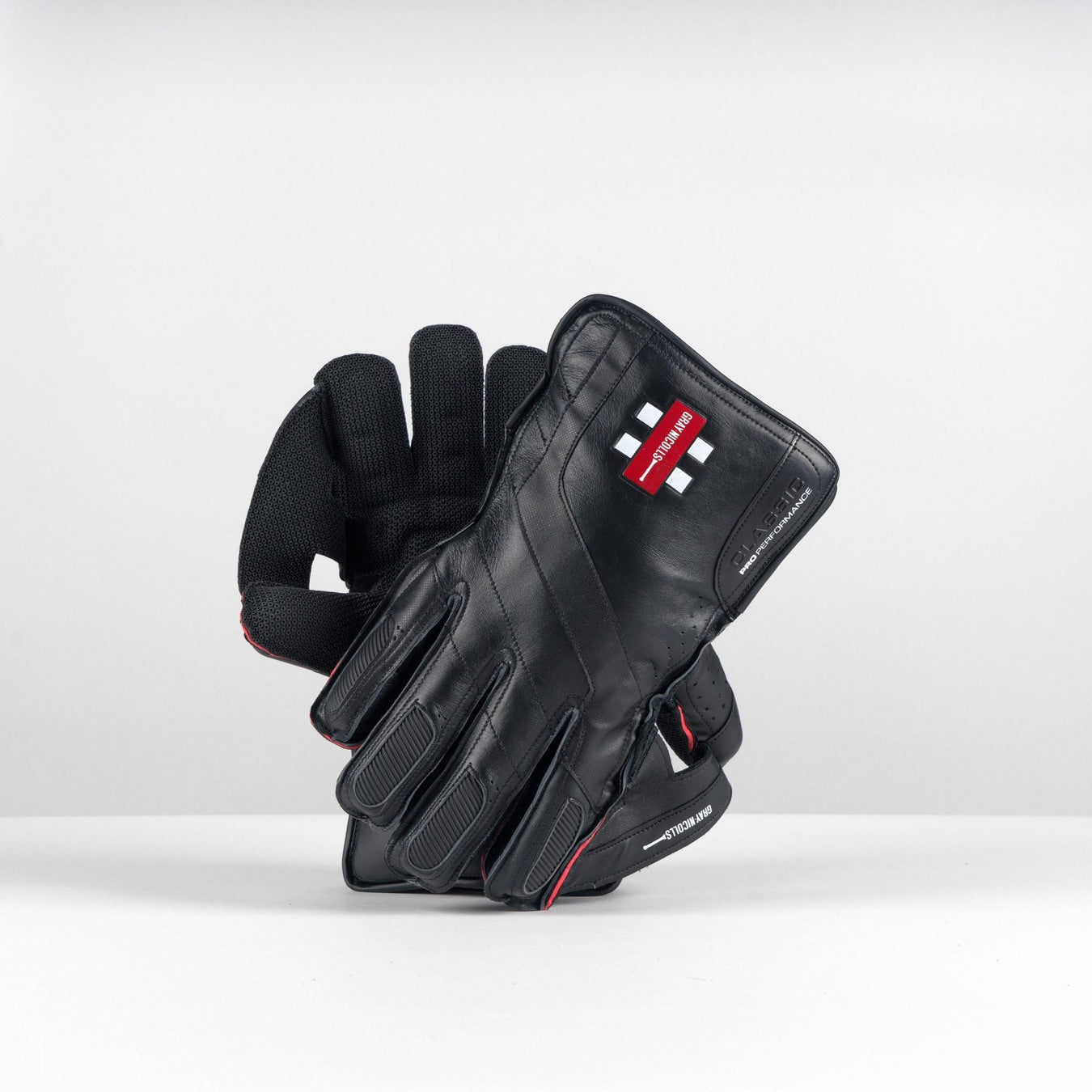 The Gray Nicolls Classic Pro Performance WK Gloves 2026 by Gray Nicolls are black, featuring Grade A leather, padding for comfort, and a palm with an octopus grip and textured surface. They are displayed upright on a white surface against a light grey background.
