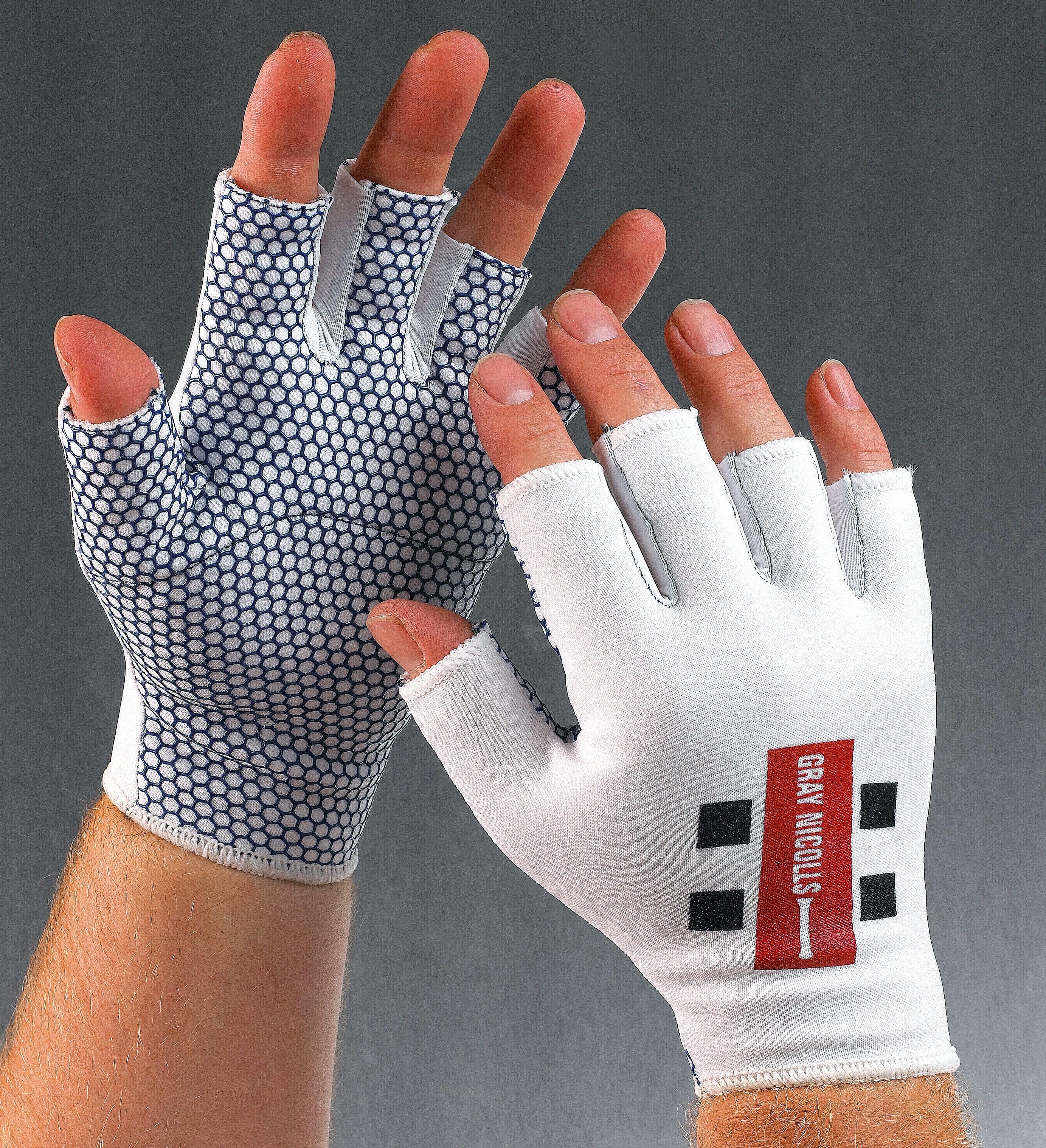 Two hands wear Gray Nicolls Catching Gloves. The palms have a black and white hexagonal grip pattern, while the backs are white with a red and black Gray Nicolls logo. Background is gray.