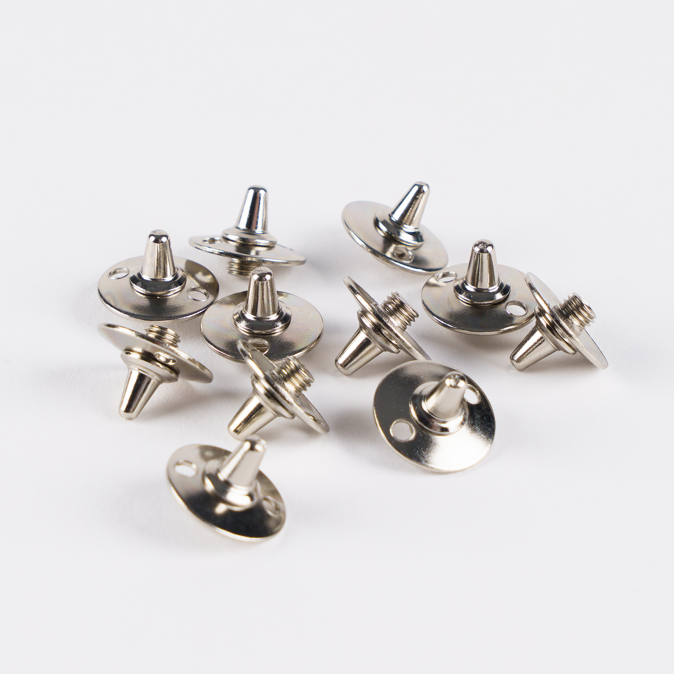 A set of 20 Gray Nicolls Steel Spikes, featuring shiny metal construction with round bases and threaded posts, are scattered on a white surface.