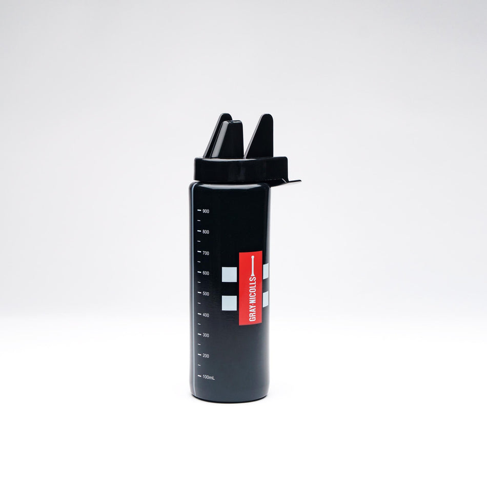 The Gray Nicolls Pro Water Bottle, featuring a black body, red label, white measurement markings, and a unique spout lid, stands upright against a plain white background.