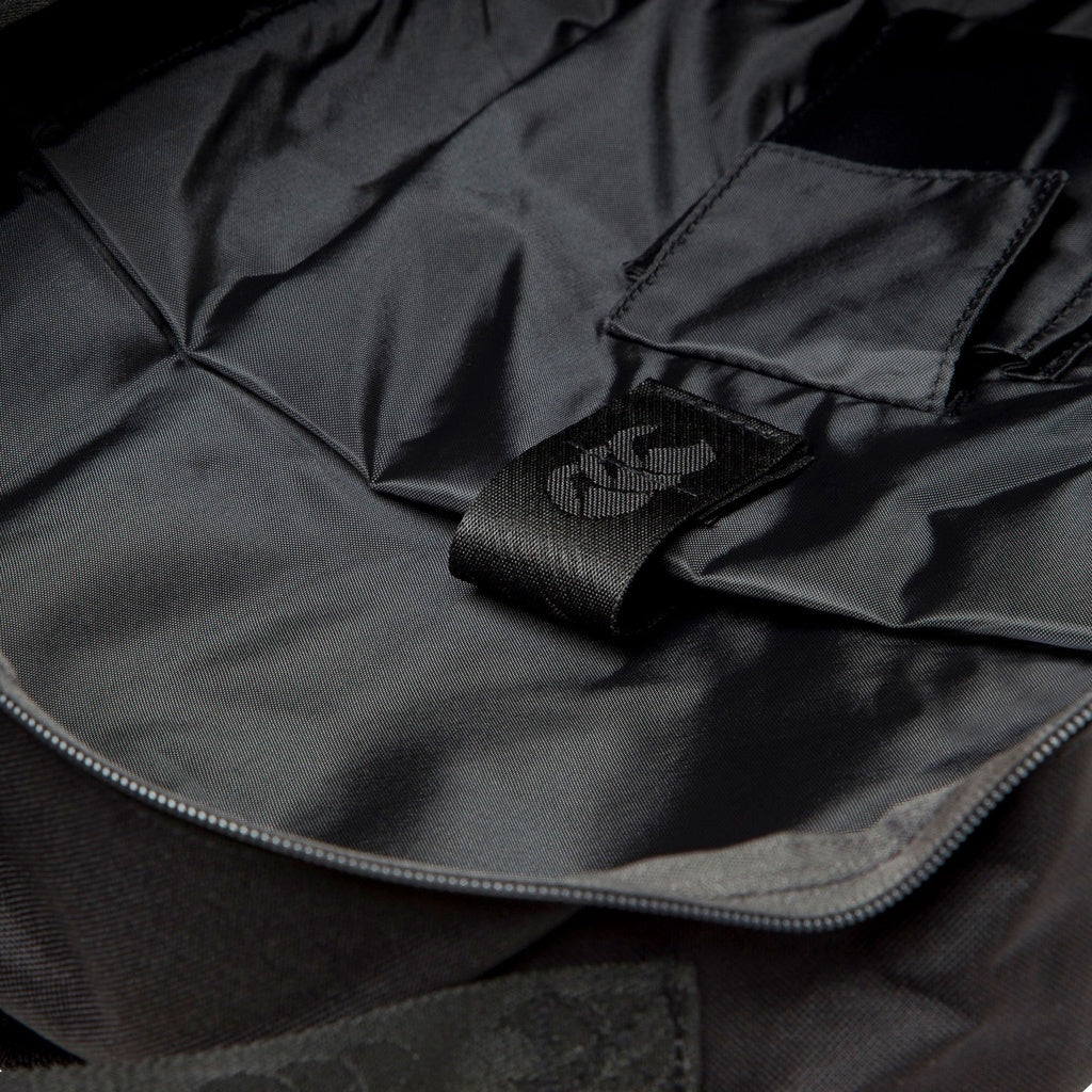 A close-up of the Canterbury Classic Backpack’s black interior reveals a stitched fabric loop with a white symbol, smooth lining, interior pockets, an ergonomic shoulder strap, and a padded laptop pocket—all by Canterbury.
