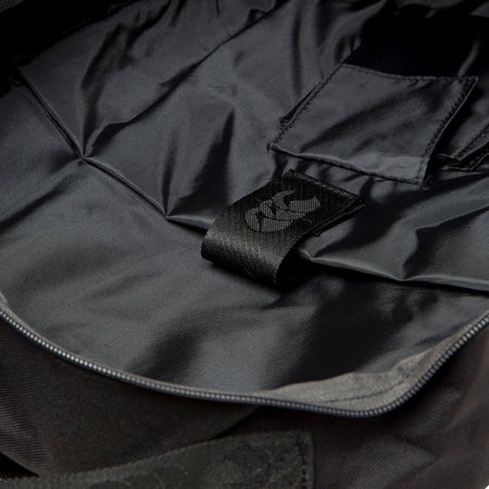 A close-up of the Canterbury Classic Backpack’s black interior reveals a stitched fabric loop with a white symbol, smooth lining, interior pockets, an ergonomic shoulder strap, and a padded laptop pocket—all by Canterbury.