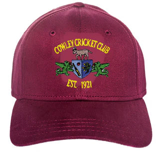 A maroon Custom Baseball Cap by Martin Berrill Sports featuring the Cowley Cricket Club crest with a goat, two green dragons, and "COWLEY CRICKET CLUB EST. 1921" in yellow. No minimum order required.